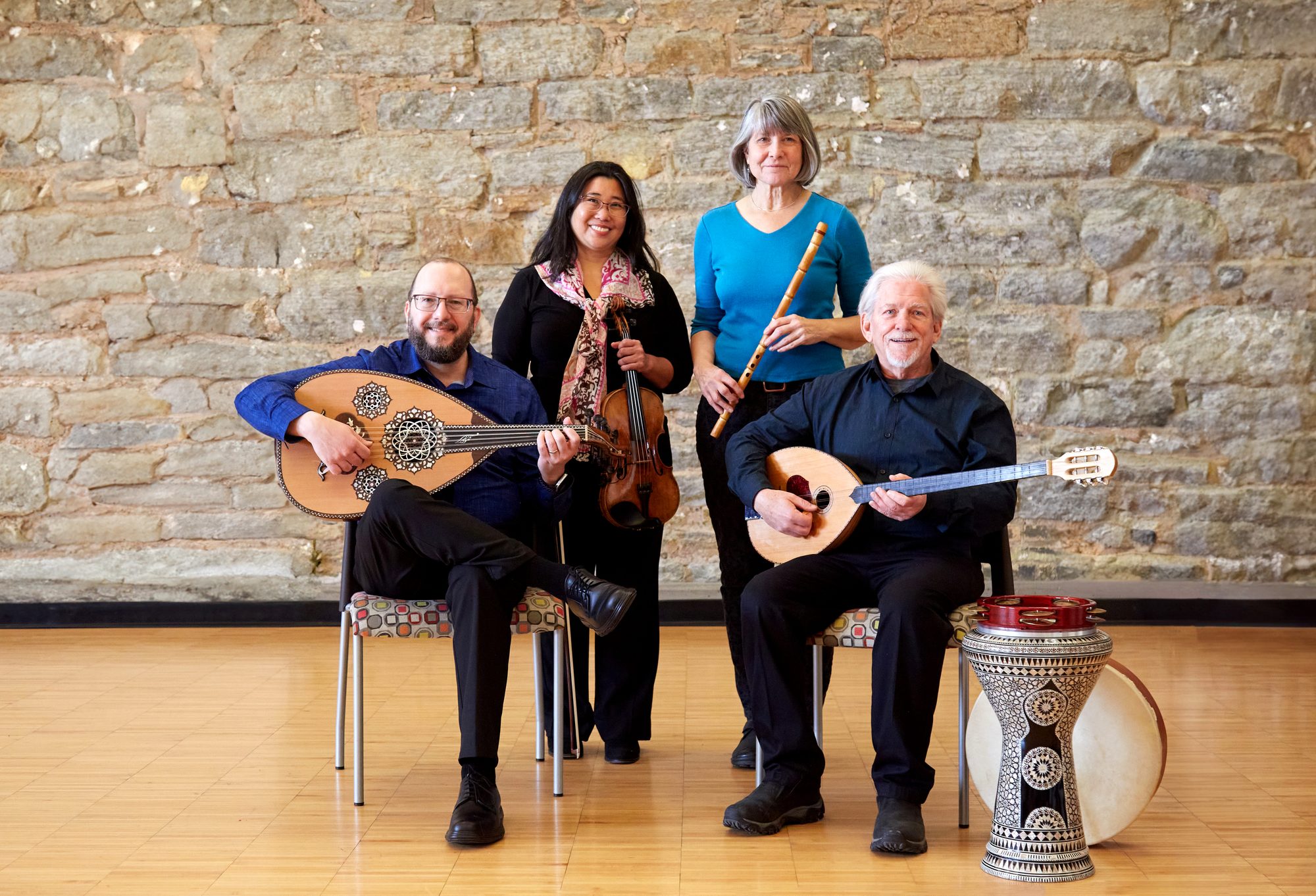 The four members of Amwaaj with oud, violin, nay, buzuq and darbuka in front of a stone wall